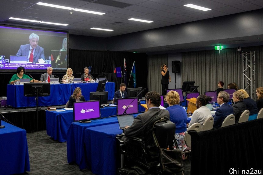 A wide shot shows inside the public hearing in Townsville led by Ronald Sackville.