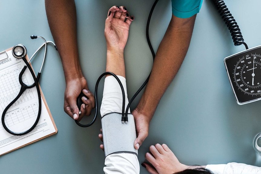 Overhead shot of doctor taking a patient's blood pressure depicting the health impacts of not looking after your mental health.