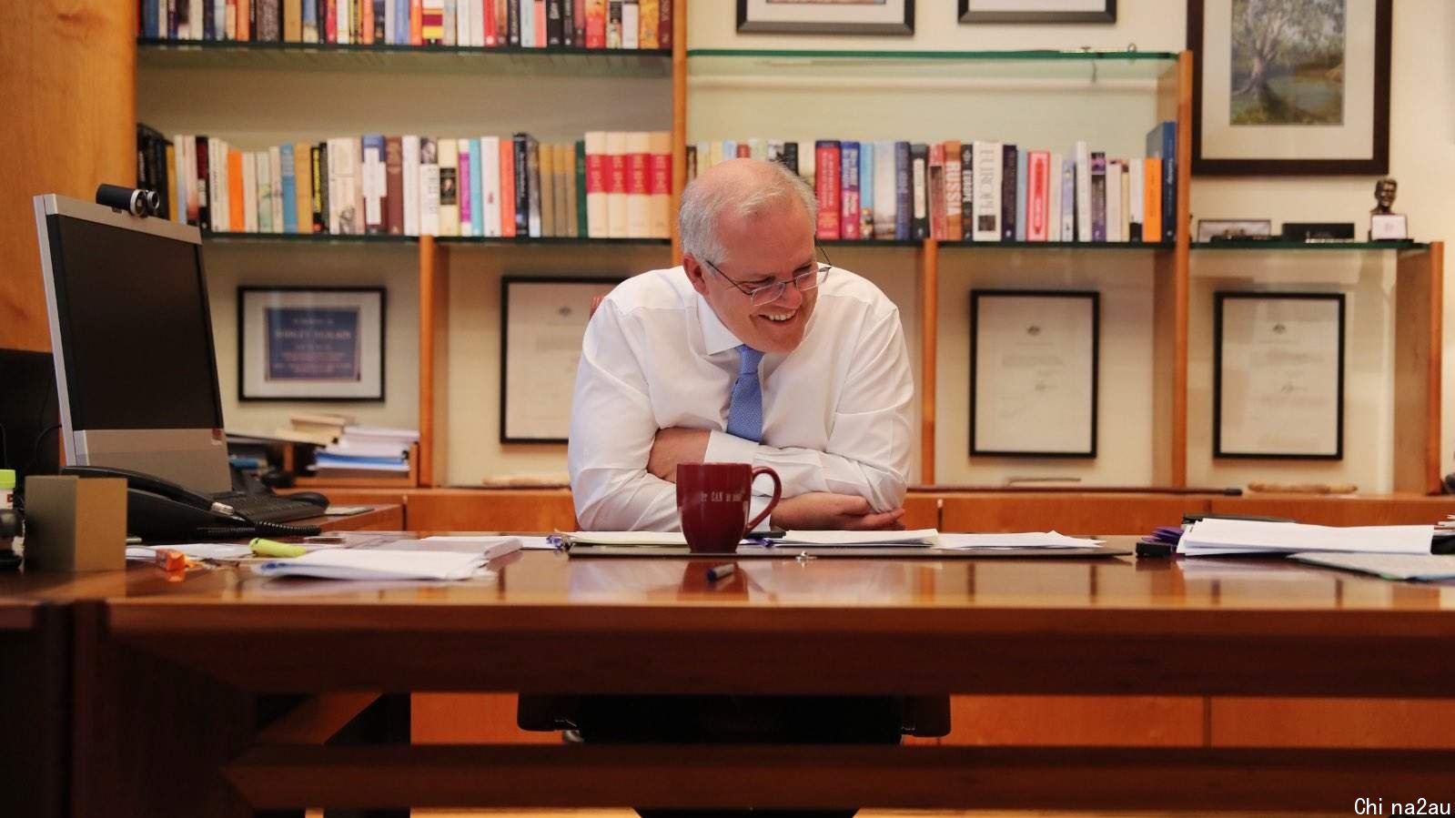 Scott Morrison sitting behind his desk with a smile on his face.