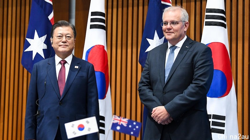 Scott Morrison and Moon Jae-in stand in front of Australian and South Korean flags. 