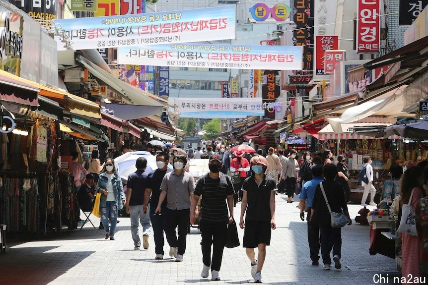 A crowd of people wearing masks while walking through a shopping strip