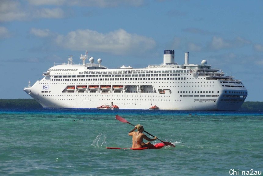 The Pacific Dawn looms large in the background, as someone paddles a canoe near the camera in the sea near Lifou island.