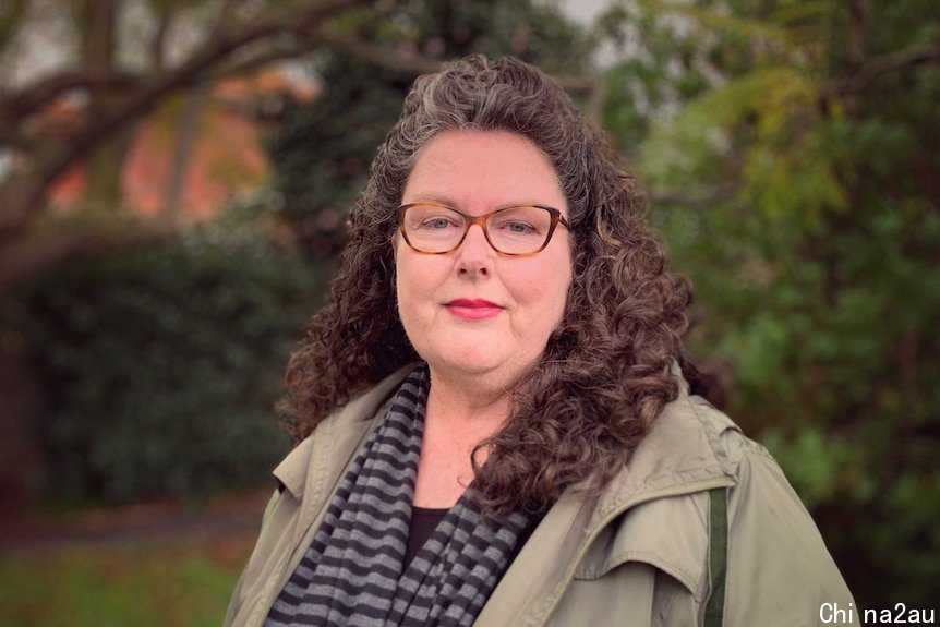 A portrait shot of a woman with a beige jacket, brown hair and glasses.