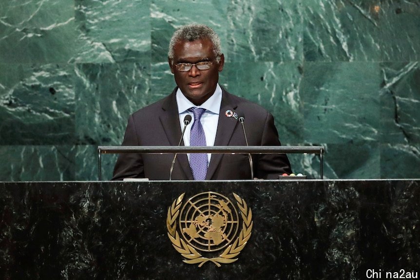 Man ina suit at a podium addresses a room full of people.