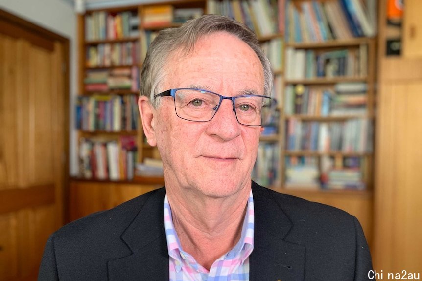 Professor Peter Collignon sits and looks into the camera with a bookcase behind him.