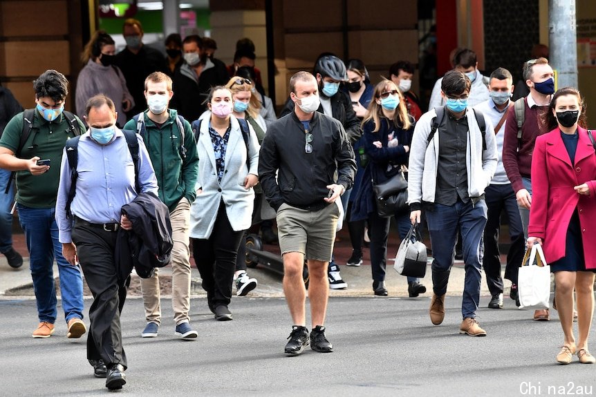 Crowd of people wearing face masks walking across a scramble crossing in Brisbane CBD.