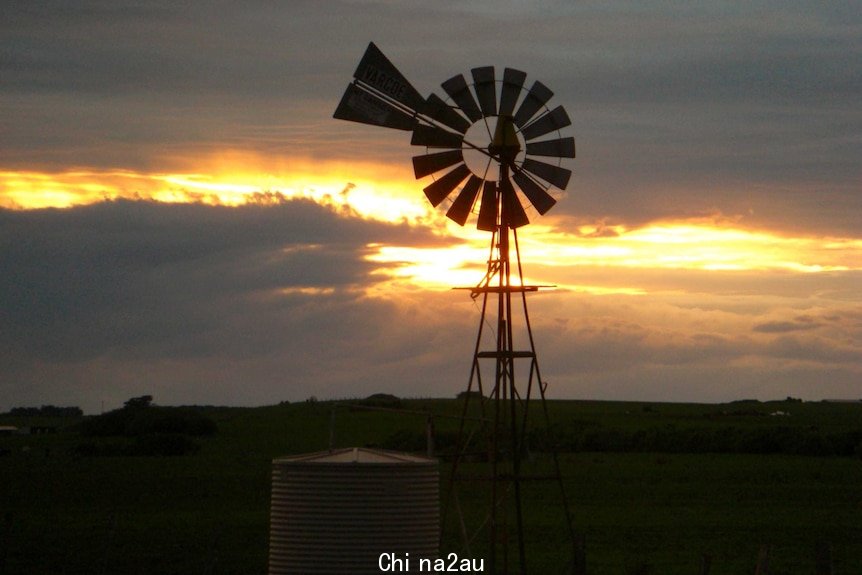 The sun sets behind a windmill on a rural property.