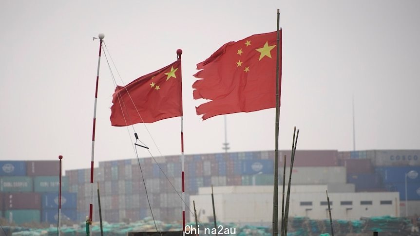 Two Chinese flags flutter in the wind at a shipping port.