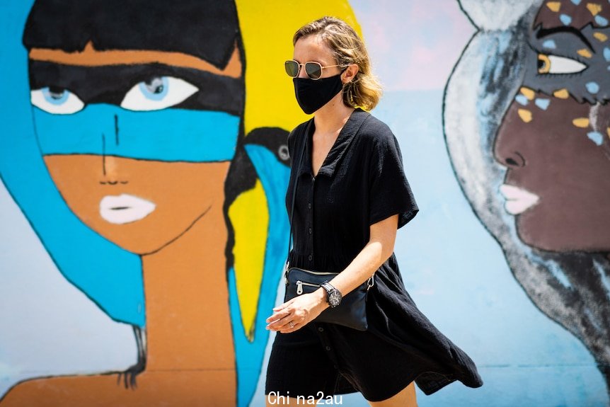 a woman wearing a face mask walking in front of street art