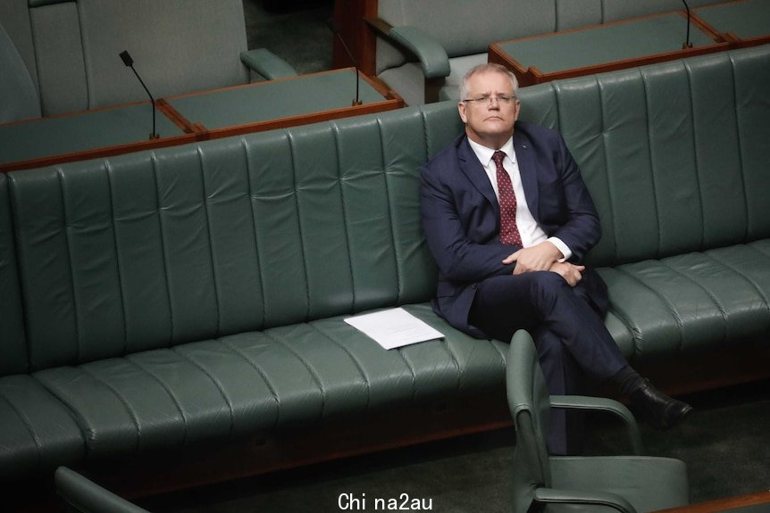 Morrison is sitting on the front bench by himself, looking upwards in a reflective pose.