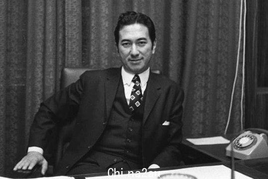 a black and white photo of a man in a suit sitting behind a desk