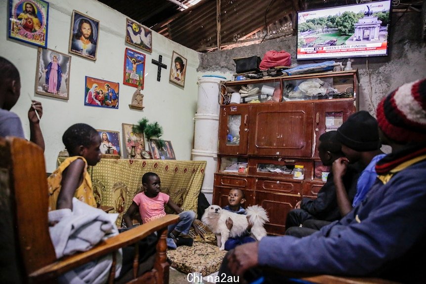 The Queen's funeral plays on a TV in a living room as children and adults watch on. 