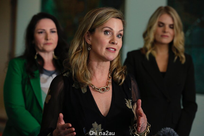 A blonde woman with shoulder length hair speaking with two other women behind her on either side