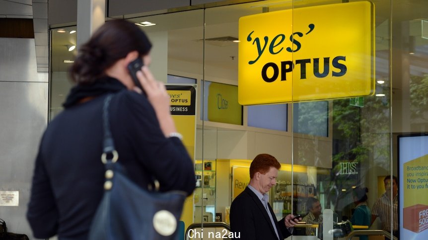 A woman uses her phone outside an Optus store as a man looks at his.