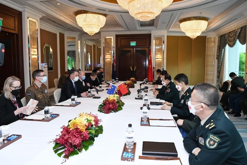 Australian officials sit across from Chinese officals at long white table adorned with the countries flags