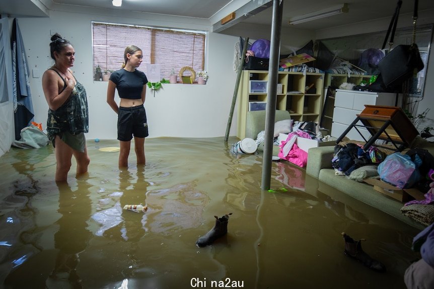 A woman and a girl wearing forlorn expressions stand in a flooded bedroom