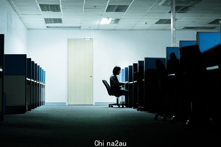 A woman sits at a computer in a dark room.