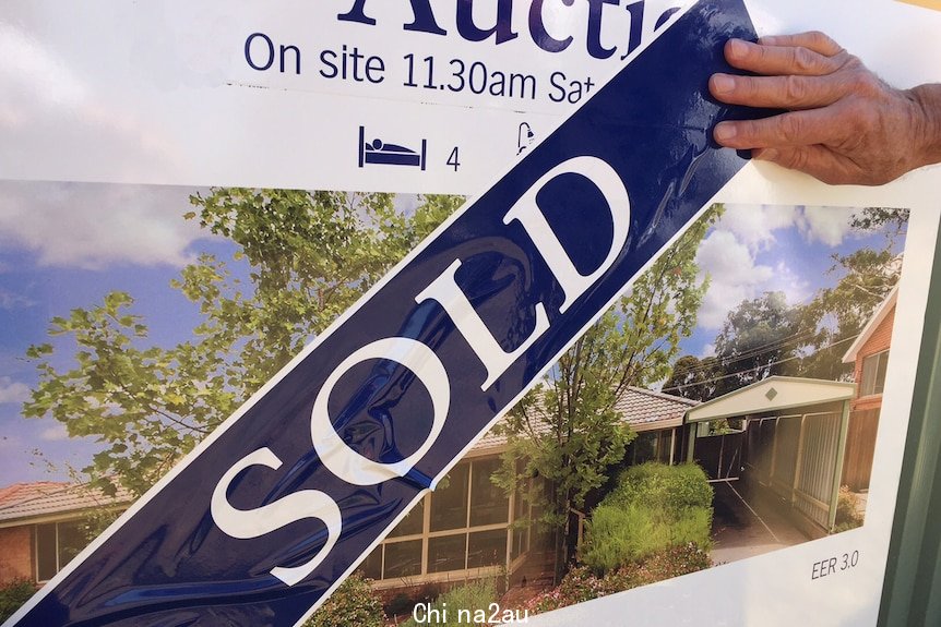 Hand touching a sold sign across an auction poster for a Sydney house.