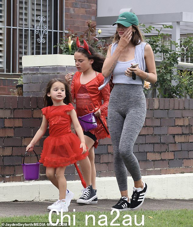 她的两个女儿穿着红色服装提着水桶收集万圣节棒棒糖