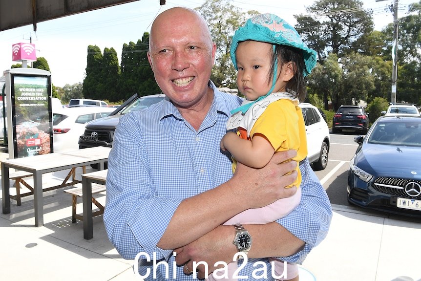 Peter Dutton 在郊区的人行道上抱着一个婴儿。