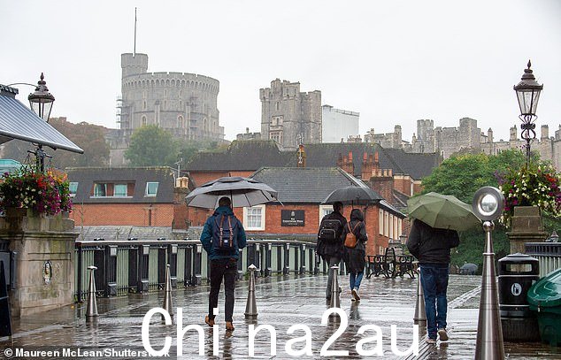 通勤者在倾盆大雨中行走，背景是温莎城堡