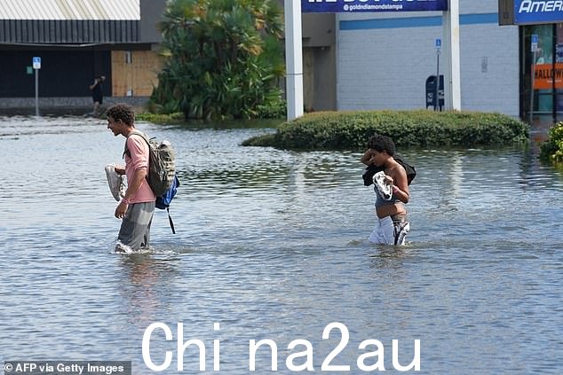 米尔顿淹没城市后，周四下午，两个人走过坦帕被洪水淹没的街道